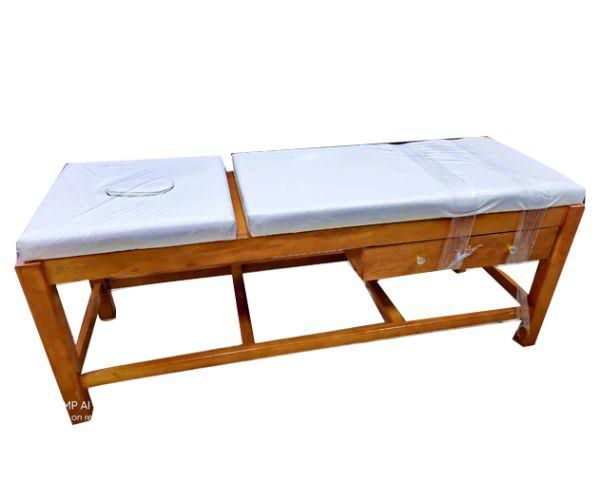 A wooden massage table with a white cushion. It has a face cradle cutout and a drawer for storage.